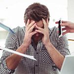 Man at computor with head in hands, lots of people giving him tasks